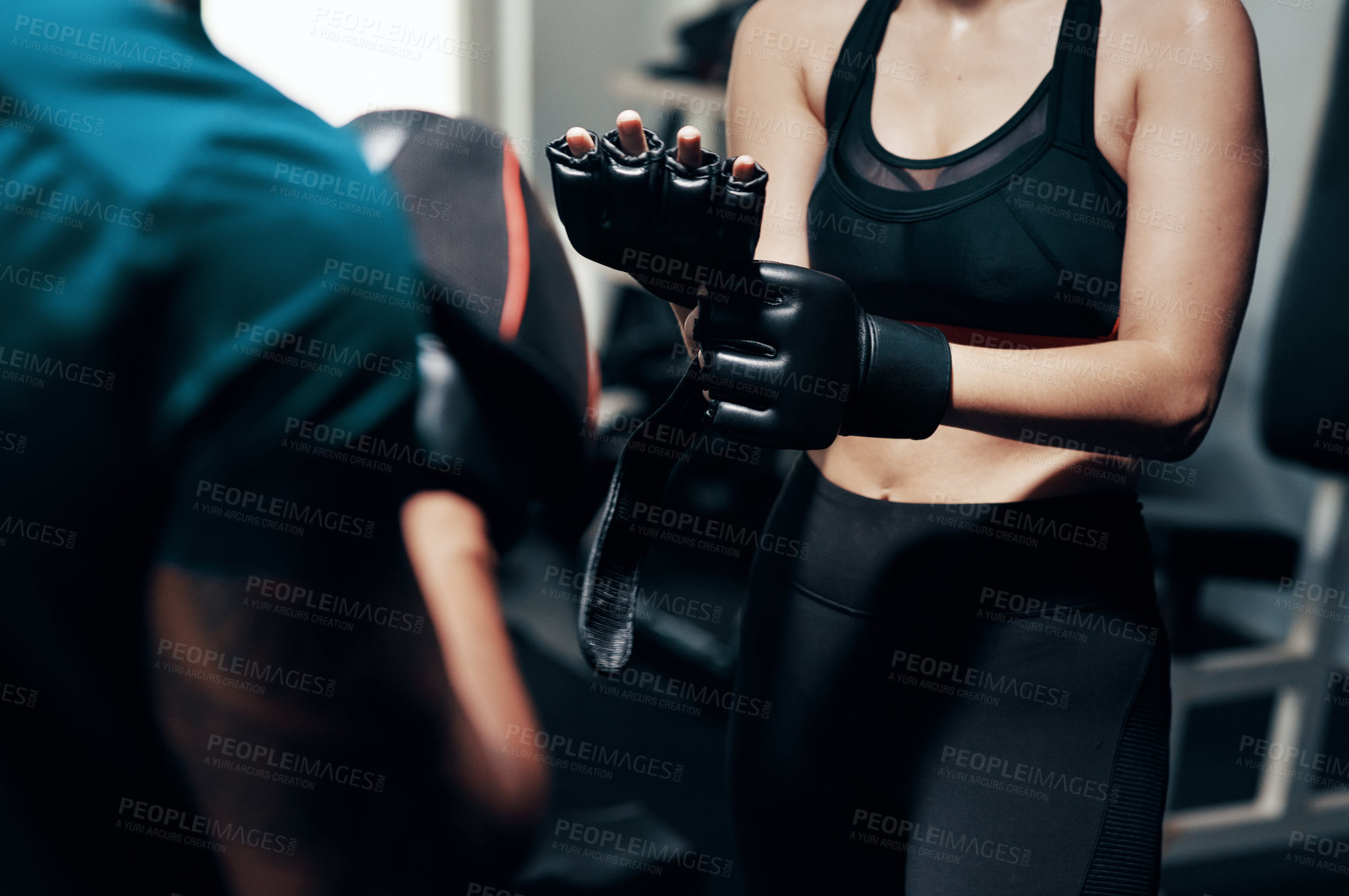 Buy stock photo Cropped shot of an unrecognizable sportswoman putting on protective gloves while working out with her personal trainer in a gym