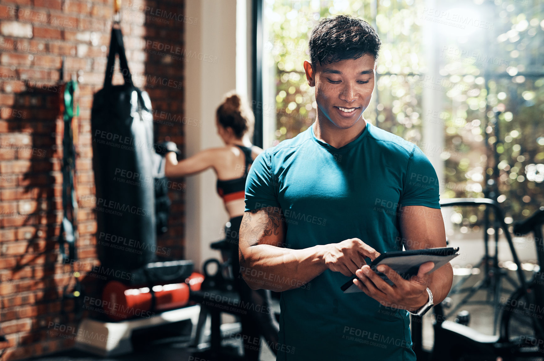 Buy stock photo Cropped shot of a handsome young sportsman using a digital tablet in a gym with his fitness partner in the background