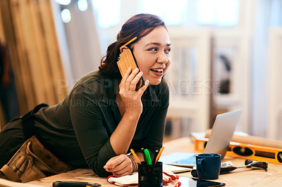 Buy stock photo Shot of a female carpenter talking on her cellphone while leaning over her desk