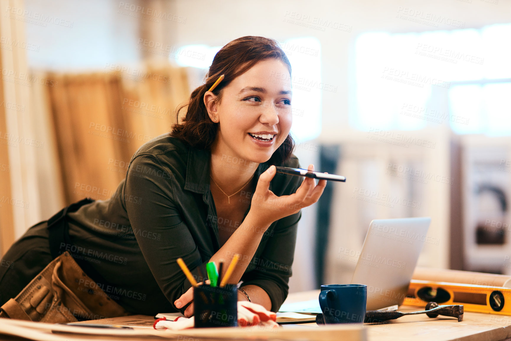 Buy stock photo Cropped shot of a female carpenter using her cellphone while leaning over her desk