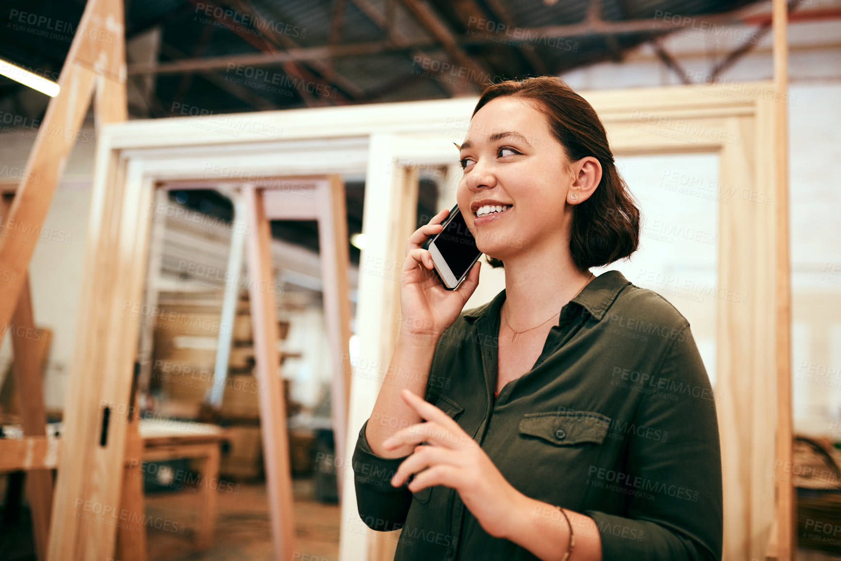 Buy stock photo Shot of a female carpenter talking on her cellphone while standing in her workshop