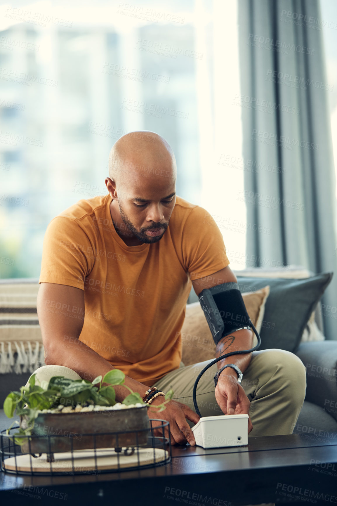 Buy stock photo Shot of a young man taking his blood pressure while sitting on the sofa at home