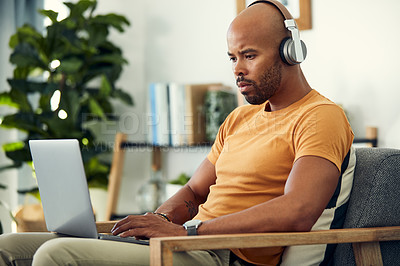 Buy stock photo Shot of a man wearing his headphones while using a laptop at home