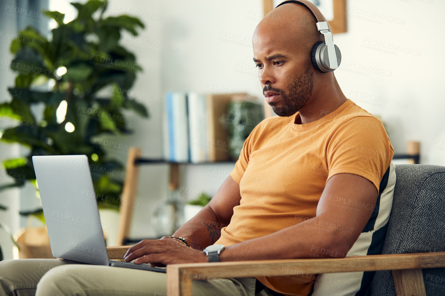 Buy stock photo Shot of a man wearing his headphones while using a laptop at home