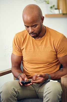 Buy stock photo Shot of a young man checking his blood sugar levels while sitting on the sofa at home