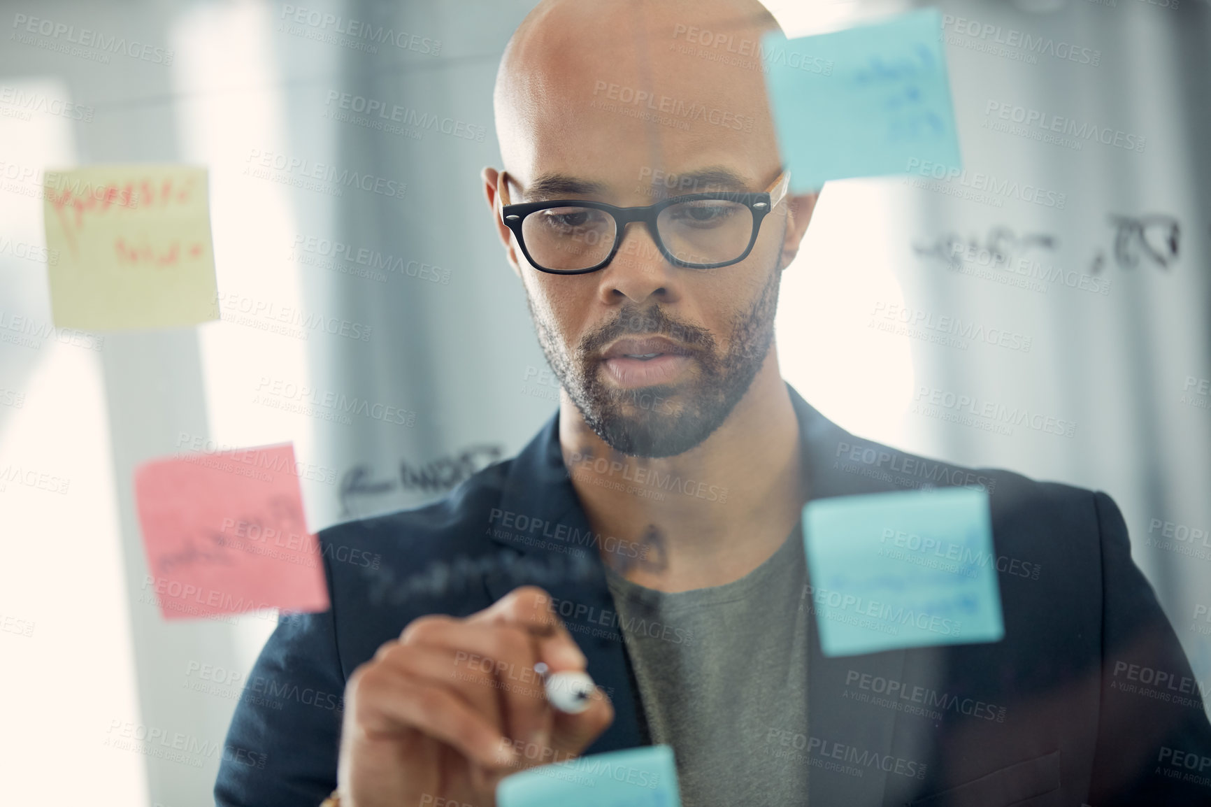 Buy stock photo Cropped shot of a young businessman brainstorming with notes on a glass wall in an office