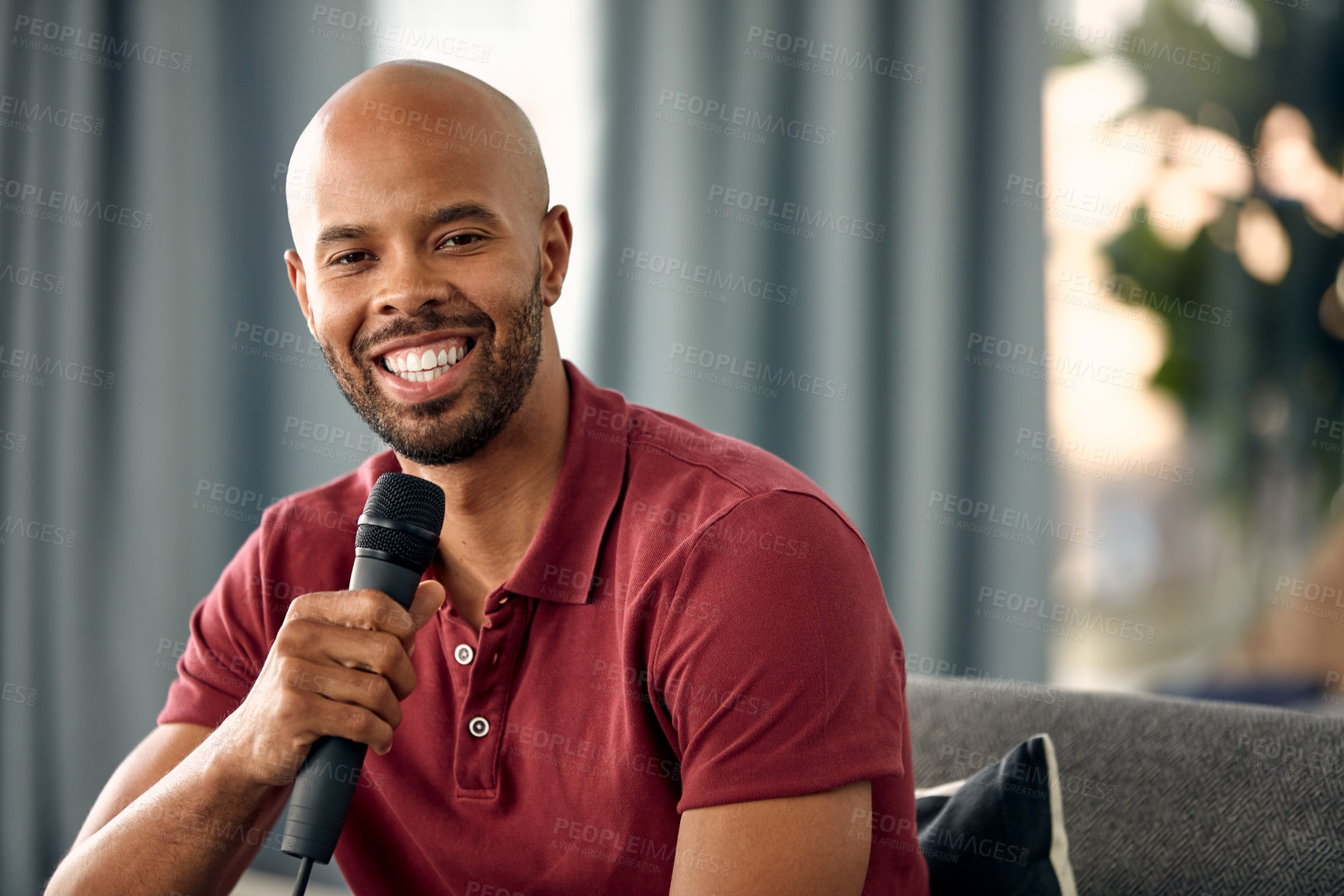 Buy stock photo Cropped shot of a young man sitting on a sofa while speaking over a microphone