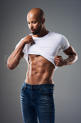 Buy stock photo Shot of a handsome young man taking off his t-shirt against a grey background