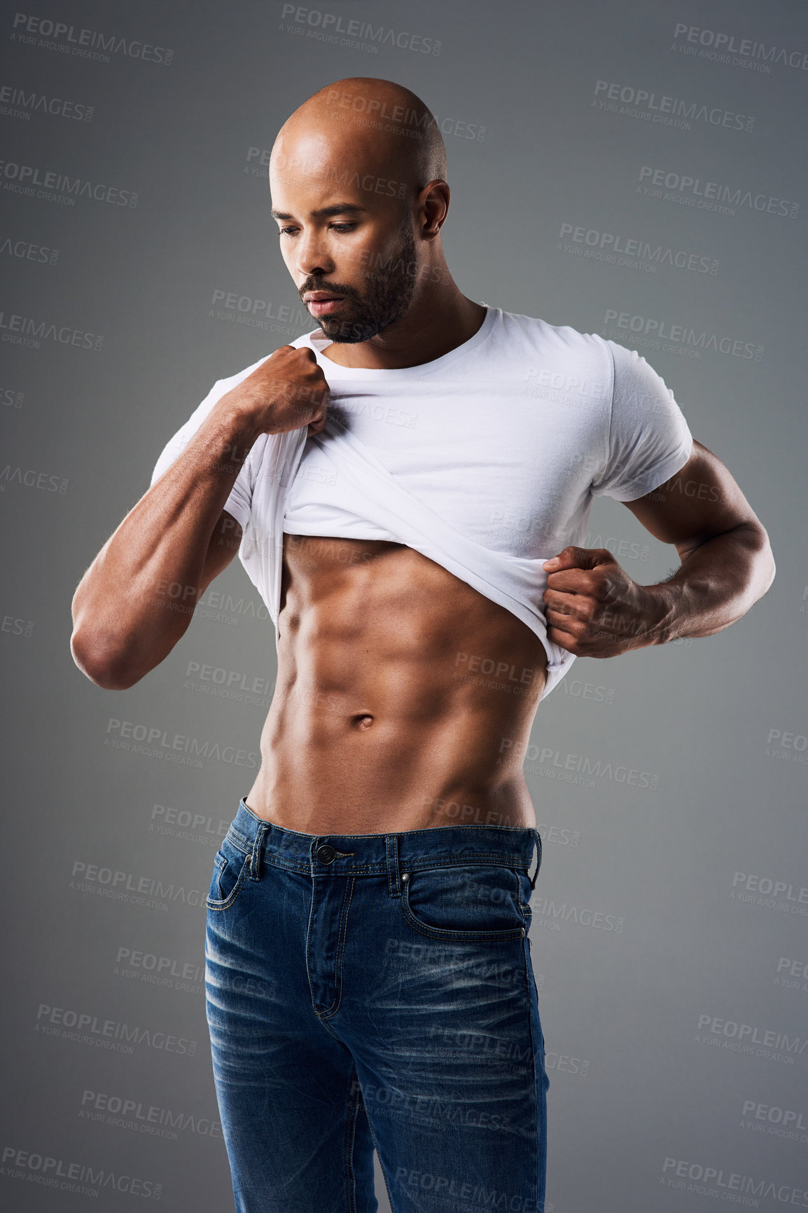 Buy stock photo Shot of a handsome young man taking off his t-shirt against a grey background