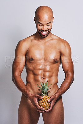 Buy stock photo Shot of a naked man posing with a pineapple covering his genital area against a grey background