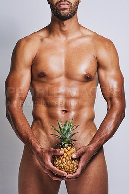 Buy stock photo Cropped shot of an unrecognizable naked man posing with a pineapple covering his genital area against a grey background