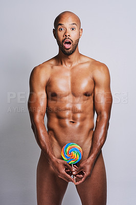 Buy stock photo Portrait of a naked man posing with a giant lollipop covering his genital area against a grey background
