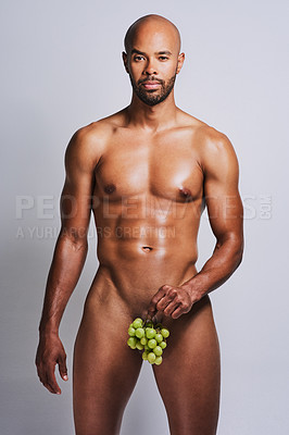 Buy stock photo Shot of a naked man posing with a bunch of grapes covering his genital area against a grey background