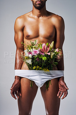 Buy stock photo Cropped shot of an unrecognizable man posing with a bouquet of flowers stuffed in his underwear against a grey background