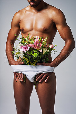 Buy stock photo Cropped shot of an unrecognizable man posing with a bouquet of flowers stuffed in his underwear against a grey background