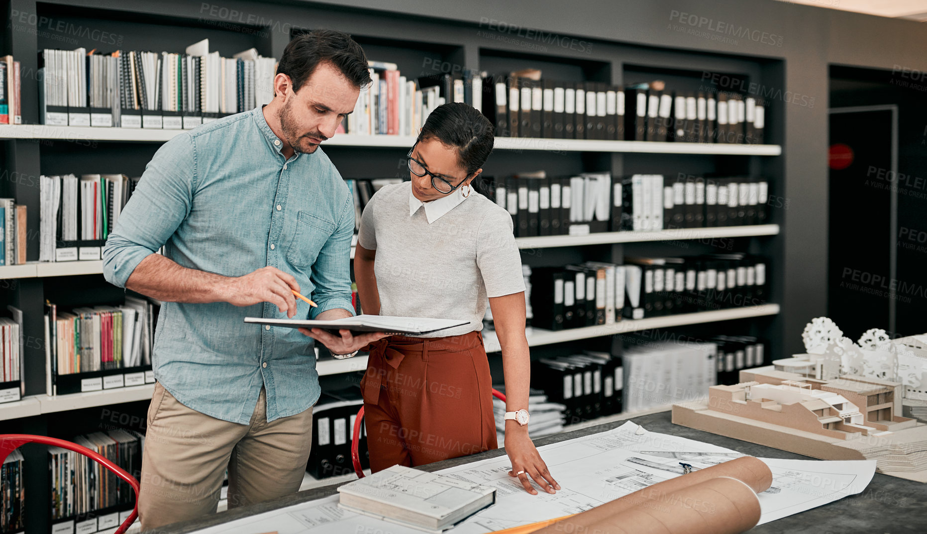 Buy stock photo Cropped shot of two aspiring young architects looking at a notebook working together in a modern office