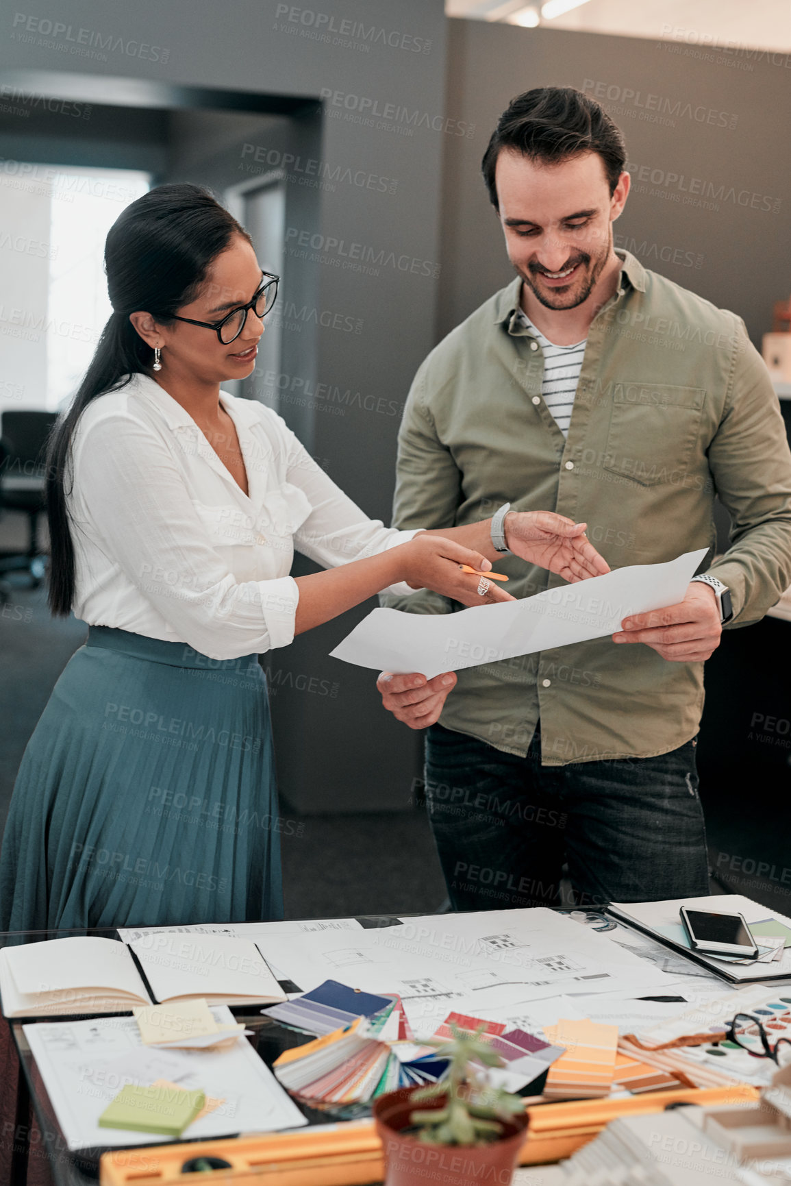 Buy stock photo Cropped shot of two aspiring young architects working with a blueprint in a modern office