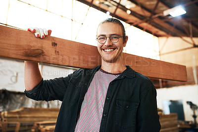 Buy stock photo Portrait of a handsome young carpenter carrying a wooden plank over his shoulders inside a workshop