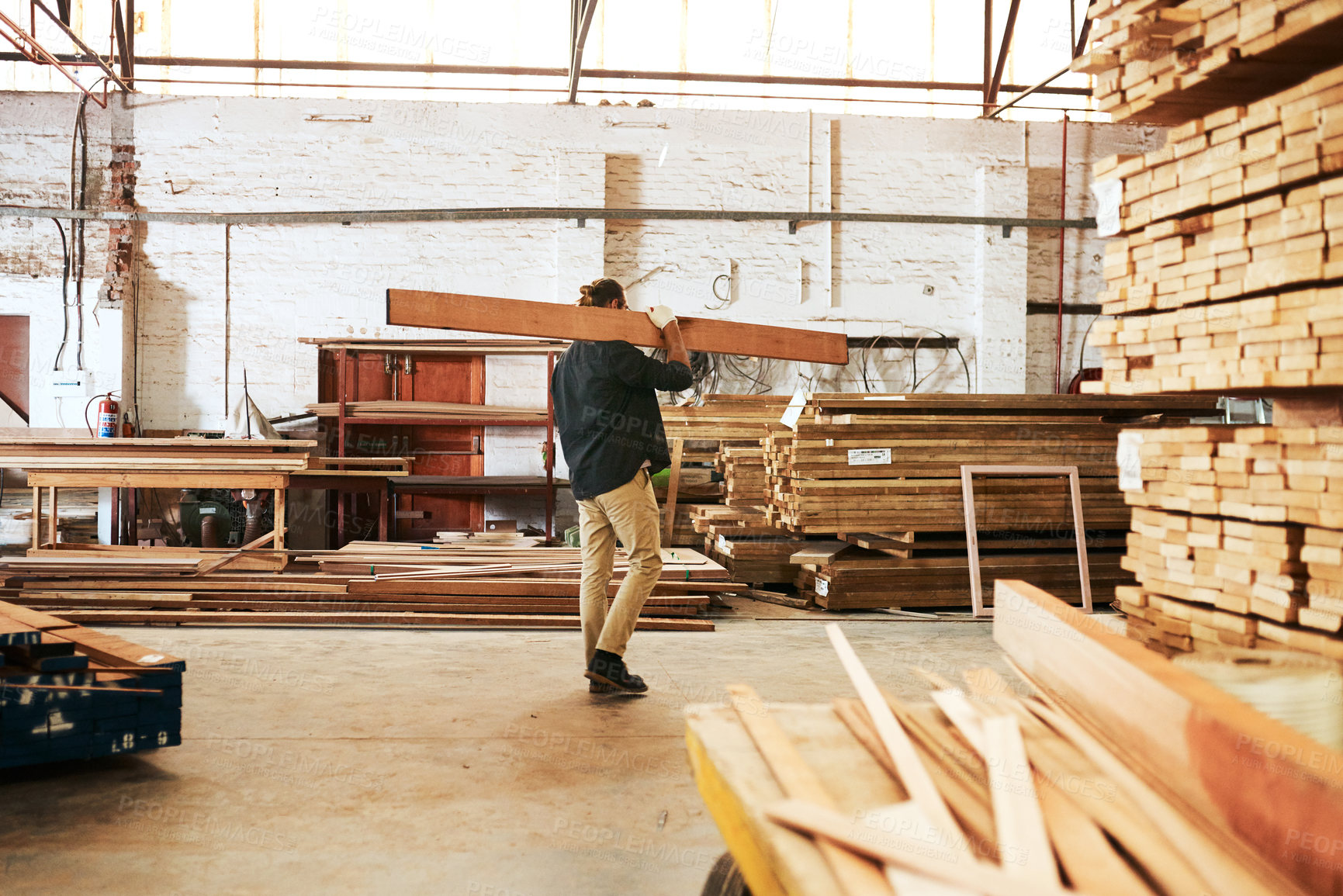 Buy stock photo Full length shot of a young carpenter carrying a wooden plank over his shoulder while working inside a workshop
