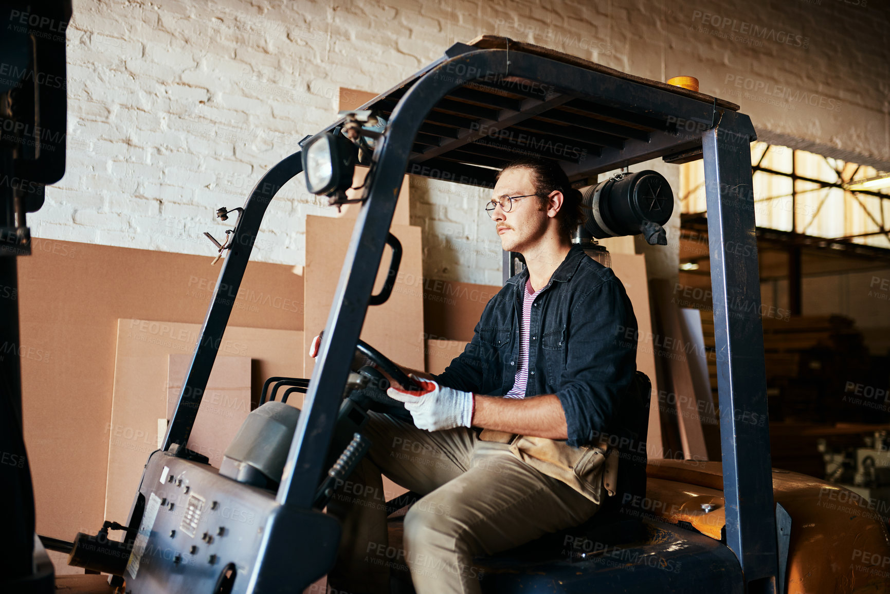 Buy stock photo Shot of a handsome young man driving a forklift inside a warehouse