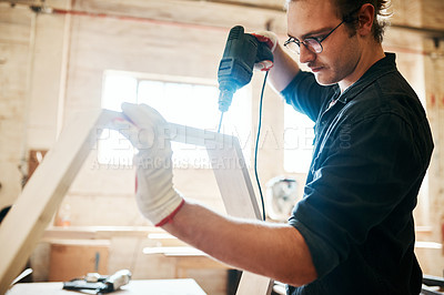Buy stock photo Shot of a handsome young carpenter using an electric drill while working inside a workshop