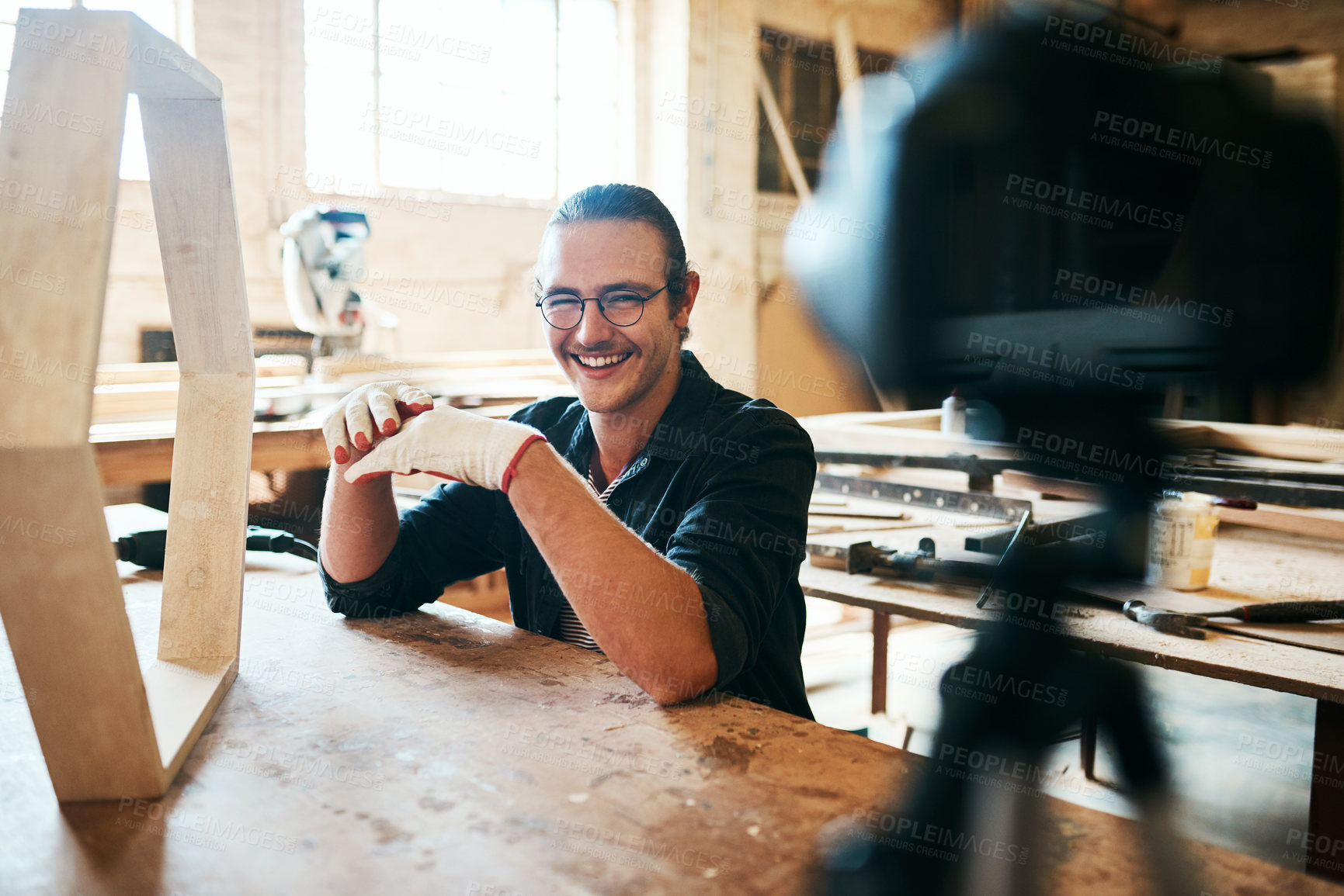 Buy stock photo Portrait of young carpenter recording a tutorial of him making a wooden masterpiece on a video camera inside his workshop