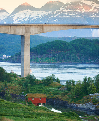Buy stock photo Landscape view of Saltstraumen Bridge in Nordland, Norway in winter. Scenery of transport infrastructure over a river or stream with a snow-capped mountain background. A remote cabin overseas 