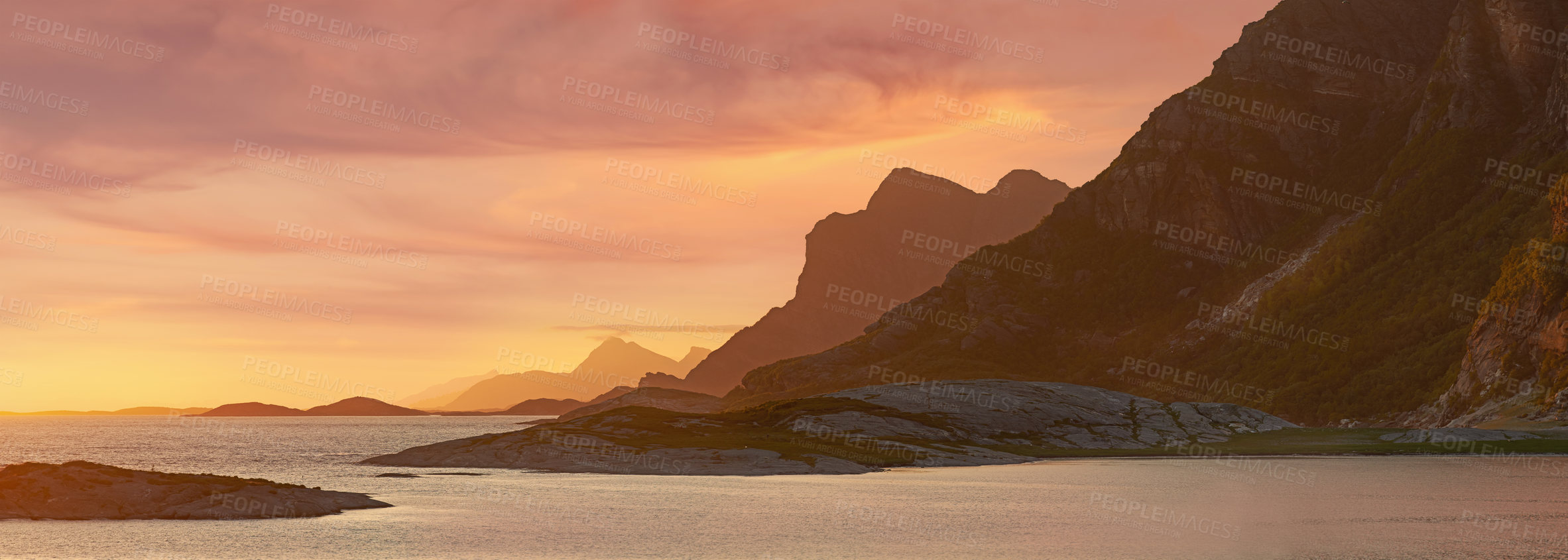 Buy stock photo The coast at sunset surrounded by mountains in nature.
Beautiful empty landscape of still ocean water or a lake on a summer evening with rocks, shrubs and grass near the mountain side 