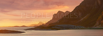 Buy stock photo The coast at sunset surrounded by mountains in nature.
Beautiful empty landscape of still ocean water or a lake on a summer evening with rocks, shrubs and grass near the mountain side 