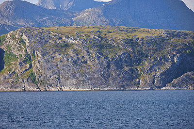 Buy stock photo The landscape of a calm sea near a rocky mountain. A range of green mountainous hills by a large lake in Norway. Peaceful ocean in a wild coastline of a Nordic nature scene for copy space