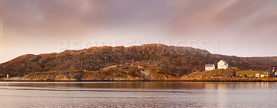 Buy stock photo Sea landscape near a mountain with houses on a hill. The ocean or a large lake with residential buildings in the distance outdoors during sunset on a cloudy day. Perfect location for summer vacation