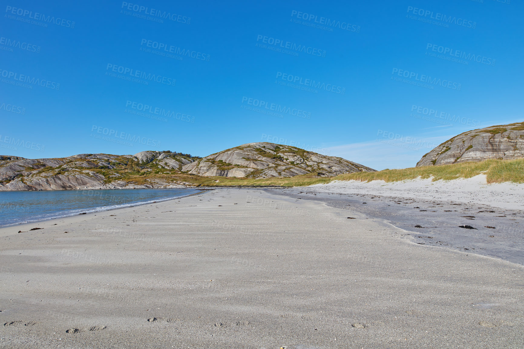 Buy stock photo Sand on an empty beach with blue sky copy space. Beautiful landscape of a scenic ocean coastline with rocky Mountains or hills in the horizon on a clear summer day with copyspace