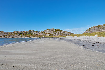 Buy stock photo Sand on an empty beach with blue sky copy space. Beautiful landscape of a scenic ocean coastline with rocky Mountains or hills in the horizon on a clear summer day with copyspace