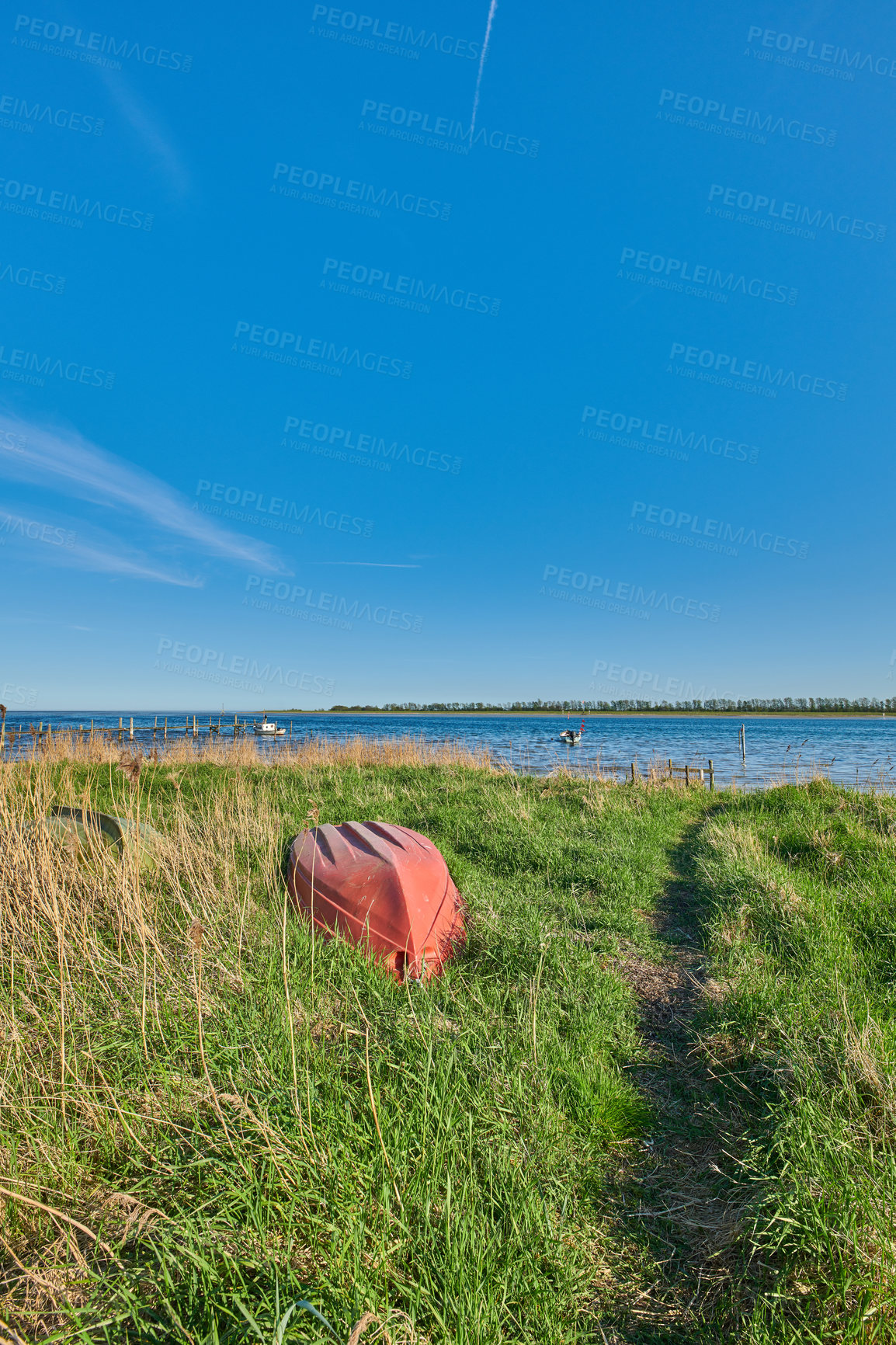 Buy stock photo Old abandoned wooden fishing boat in a green grassy meadow with flowers, a still ocean, and a clear blue sky with copy space in the background. Landscape of small boat in a remote nature environment 