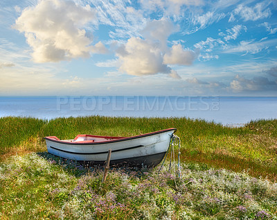 Buy stock photo Old abandoned wooden fishing boat in a green grassy meadow with flowers. Still ocean and a cloudy blue sky with copyspace in background. Perfect escape and adventure to a tranquil and remote island