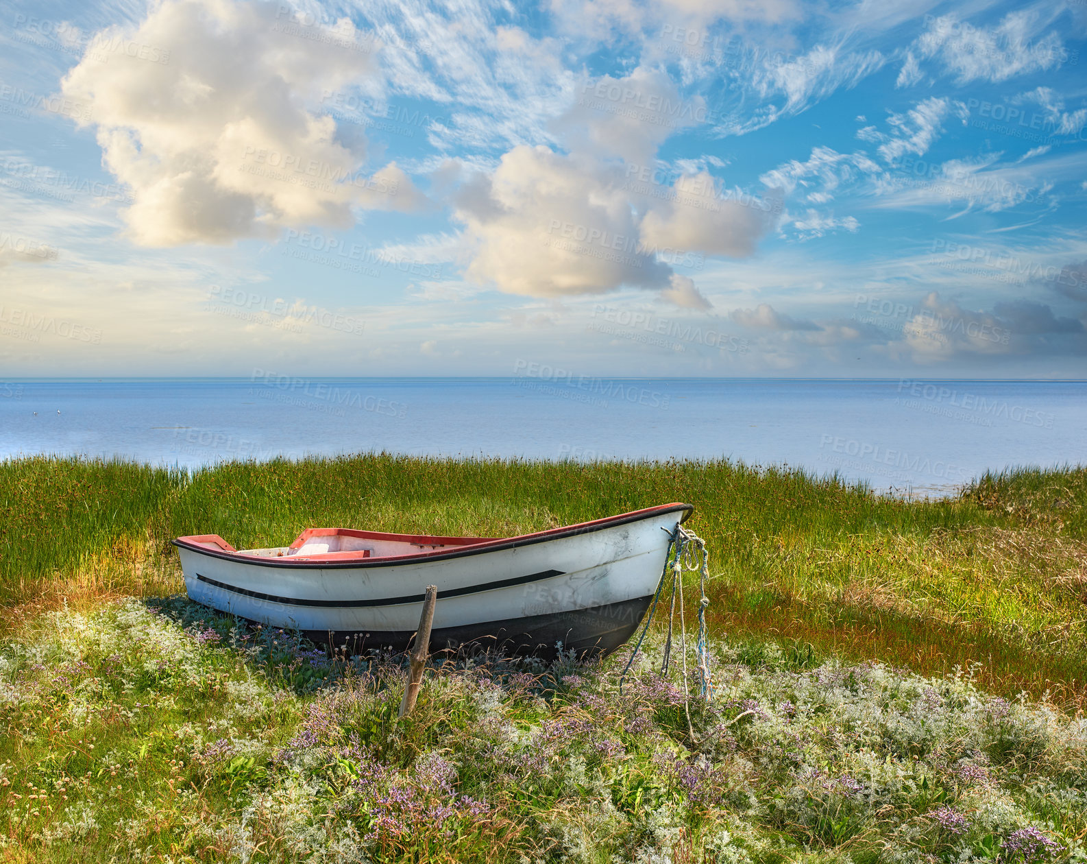 Buy stock photo Old abandoned wooden fishing boat in a green grassy meadow with flowers. Still ocean and a cloudy blue sky with copyspace in background. Perfect escape and adventure to a tranquil and remote island