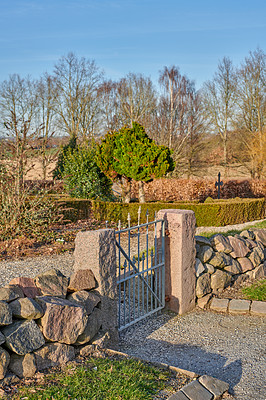 Buy stock photo A closed iron gate between two concrete pillars and stone walls at a church or park on a sunny summer day. Outdoor entrance to a house in the countryside with blue sky and pine trees in background