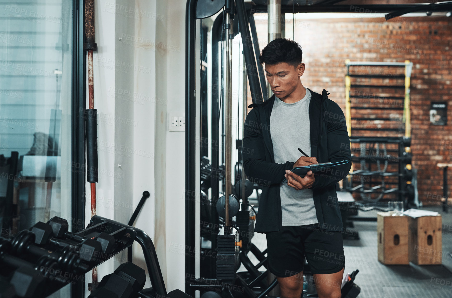Buy stock photo Cropped shot of a handsome young male fitness instructor inspecting exercise equipment while working in a gym