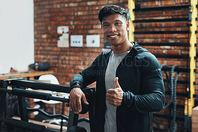Buy stock photo Cropped portrait of a handsome young male fitness instructor showing thumbs up while standing in a gym
