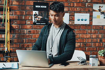 Buy stock photo Cropped shot of a handsome young male fitness instructor using a laptop while working in a gym
