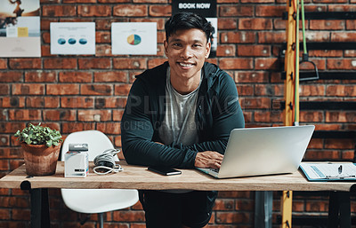 Buy stock photo Cropped portrait of a handsome young male fitness instructor using a laptop while working in a gym