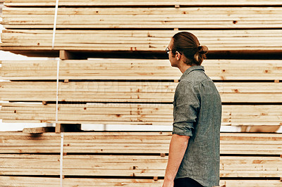 Buy stock photo Rearview shot of young carpenter looking at a piles of wood inside a workshop