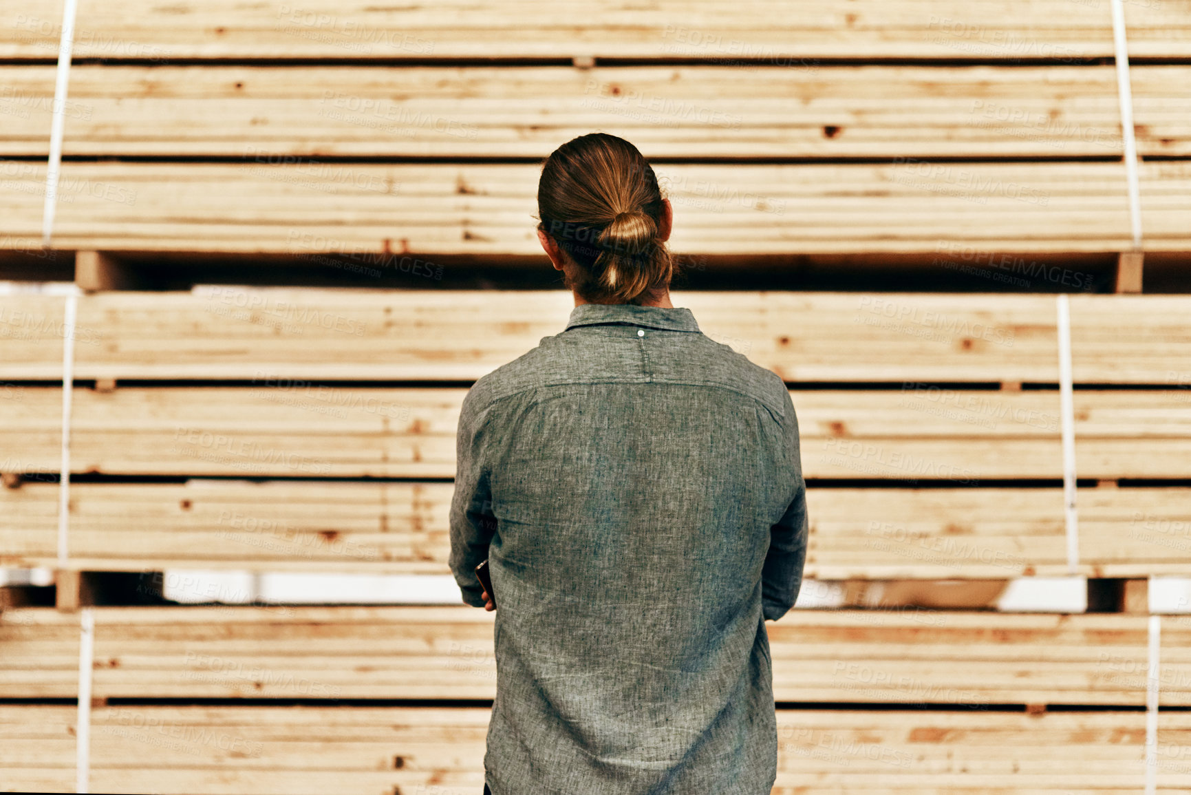 Buy stock photo Rearview shot of young carpenter looking at a piles of wood inside a workshop