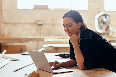 Buy stock photo Cropped shot of a young female carpenter using a laptop while working inside her workshop