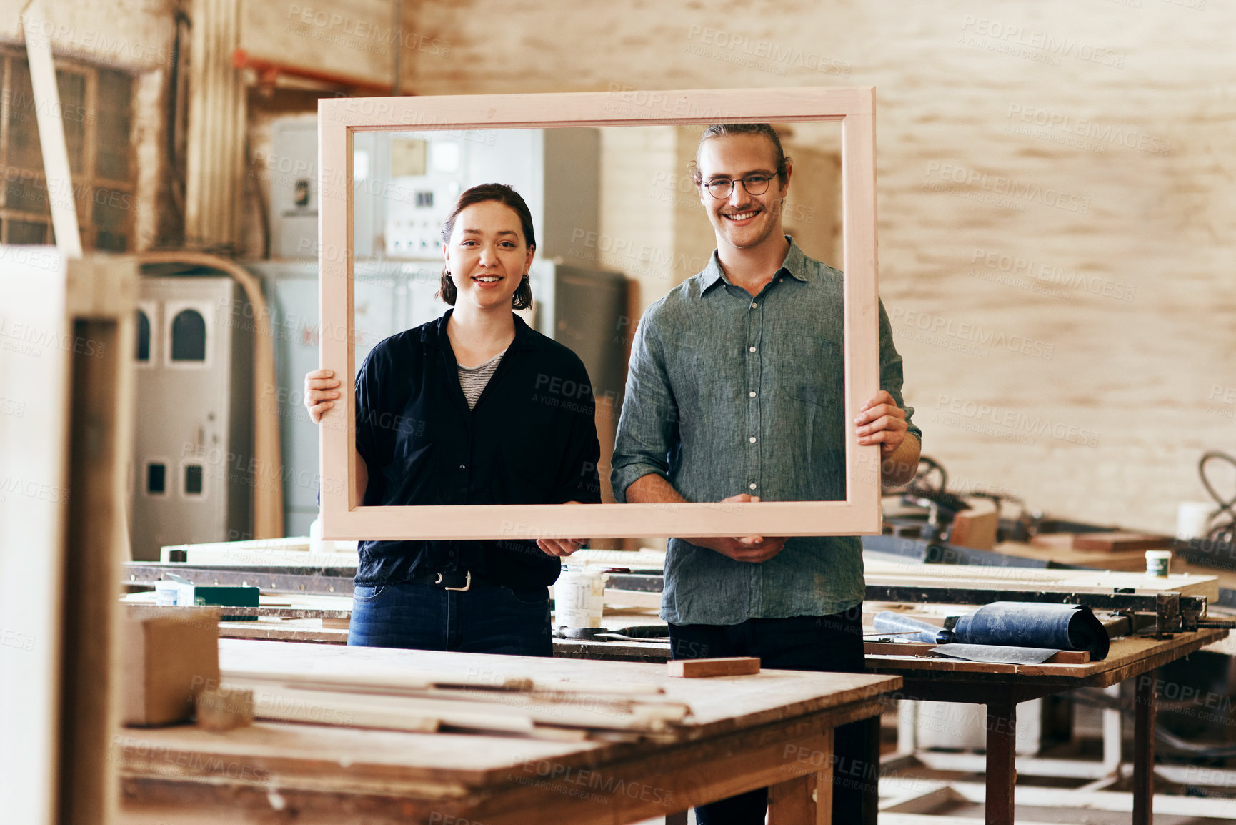 Buy stock photo Portrait of two young carpenters holding a wooden frame together inside their workshop
