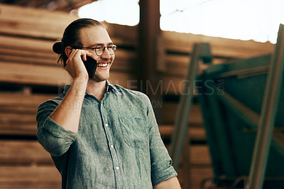 Buy stock photo Cropped shot of a young carpenter talking on a cellphone while working inside his workshop