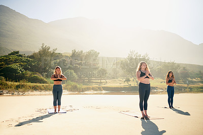 Buy stock photo Shot of three young women practicing yoga on the beach