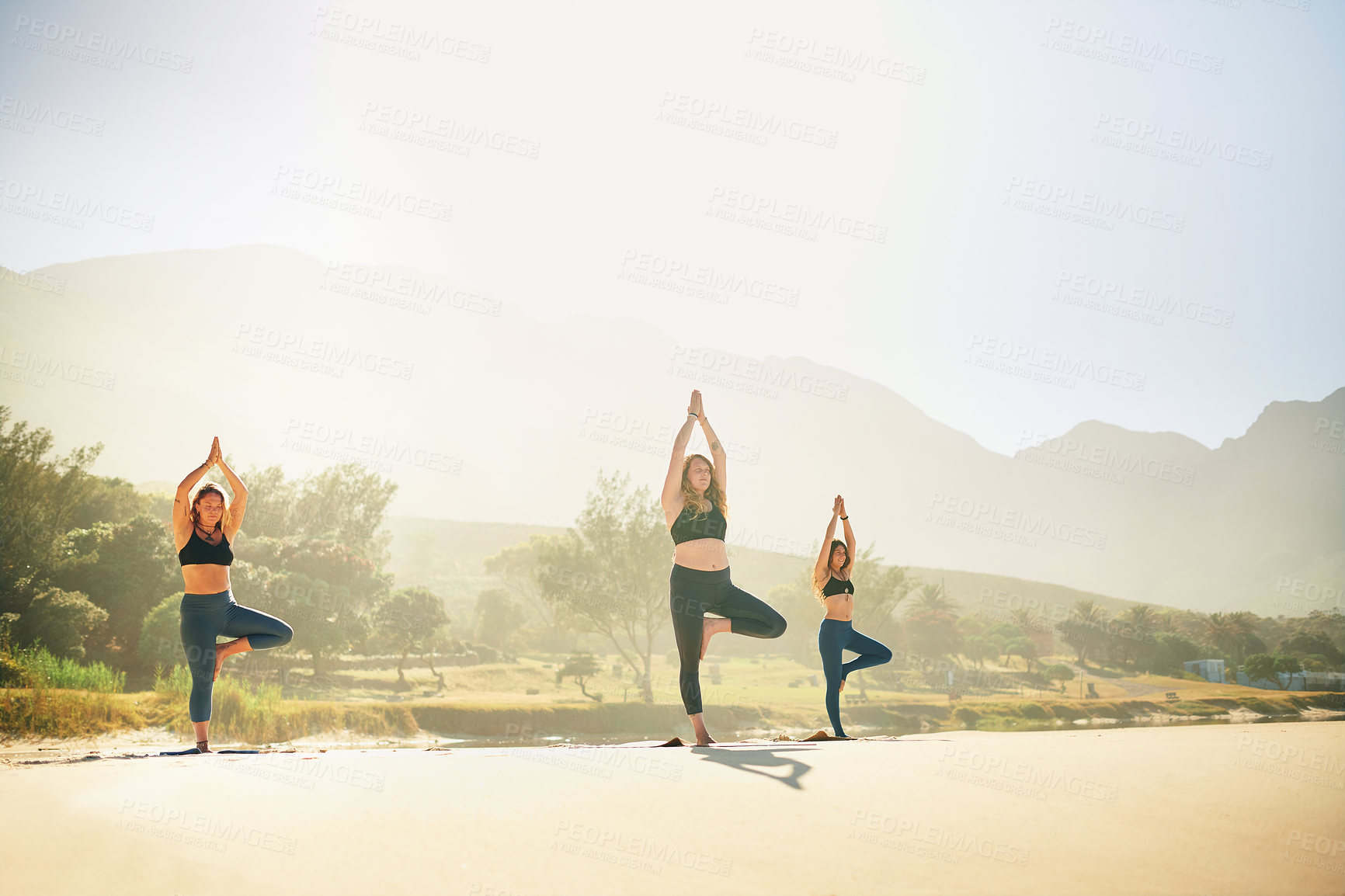 Buy stock photo Shot of three young women practicing yoga on the beach