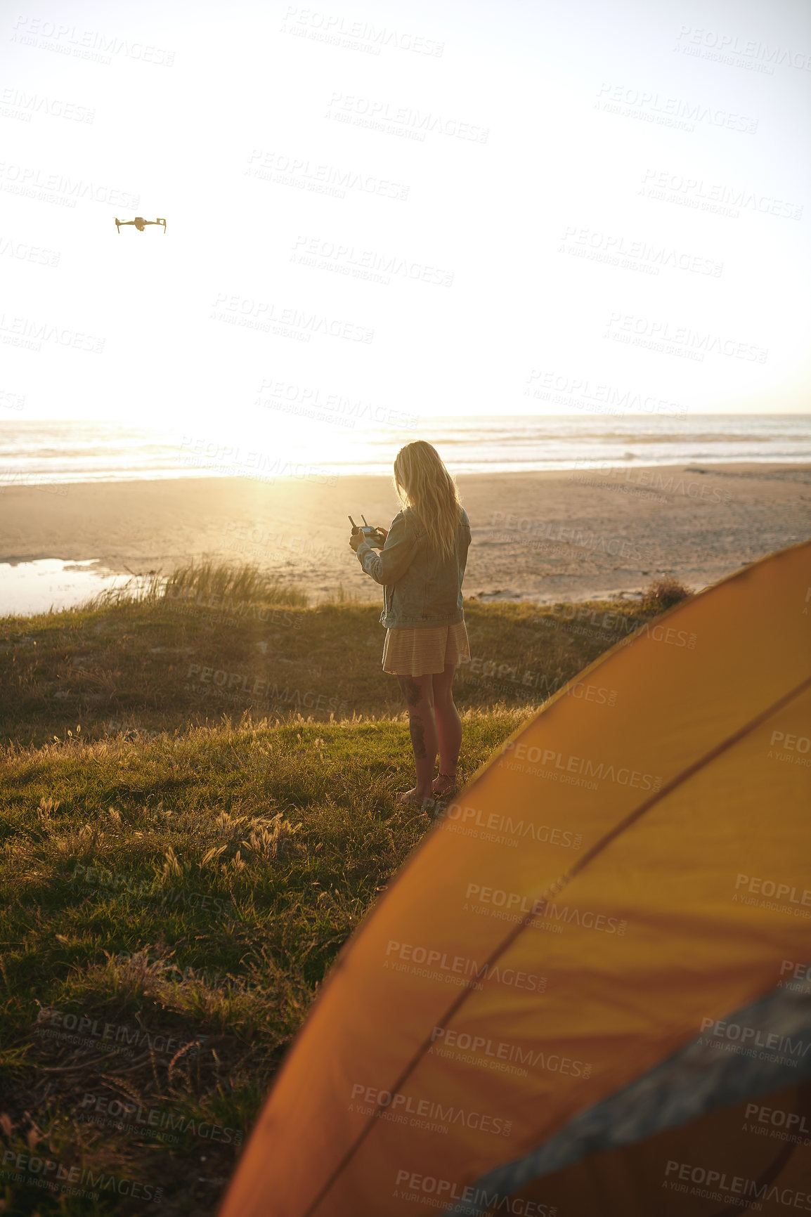 Buy stock photo Woman, remote and control a drone on beach for aerial footage of sunset and nature photography. UAV, back and robot machine by ocean for golden hour recording, fun hobby or camping with mockup space