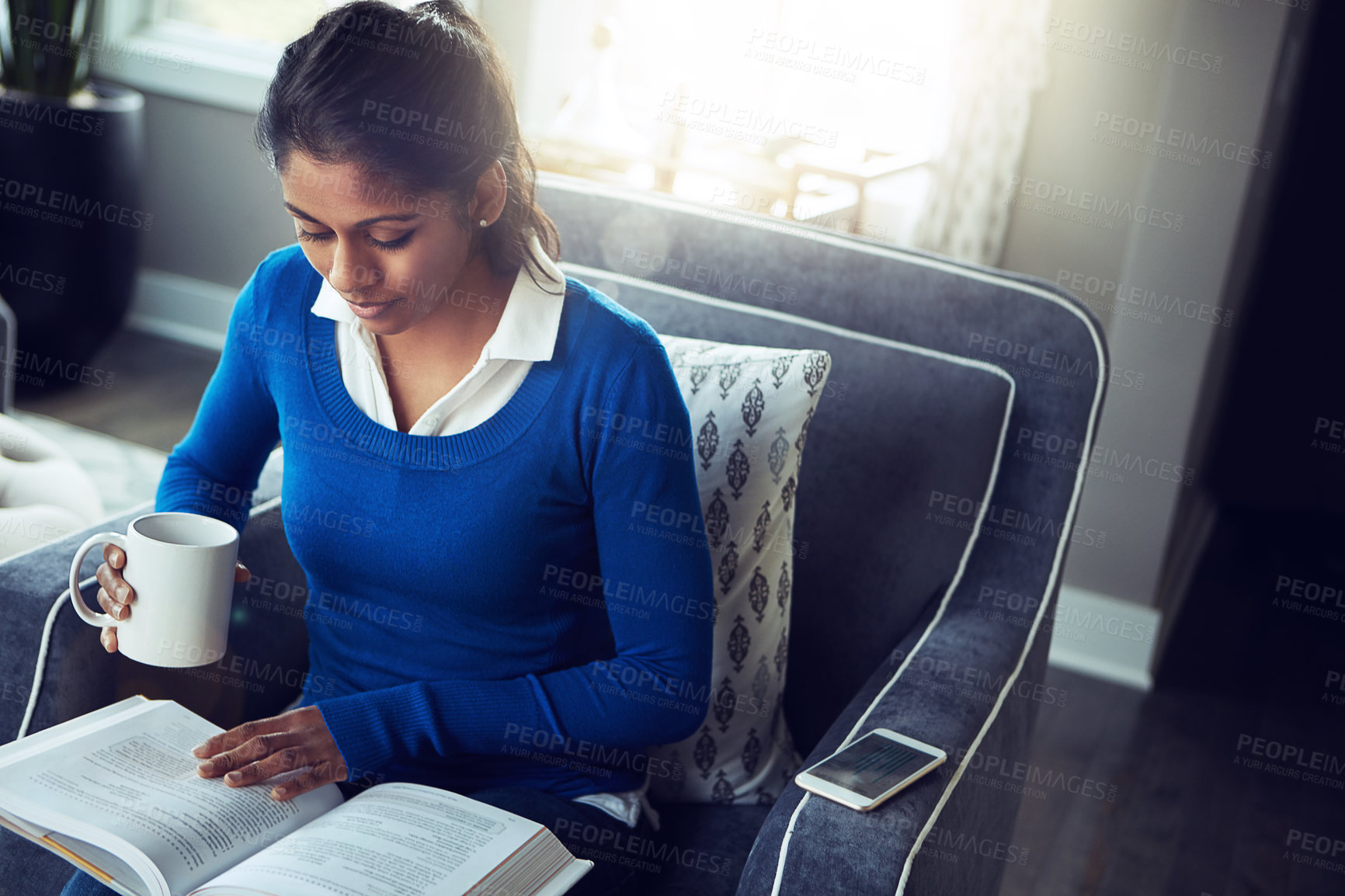 Buy stock photo Shot of a young woman relaxing on the sofa with a cup of coffee and a book at home